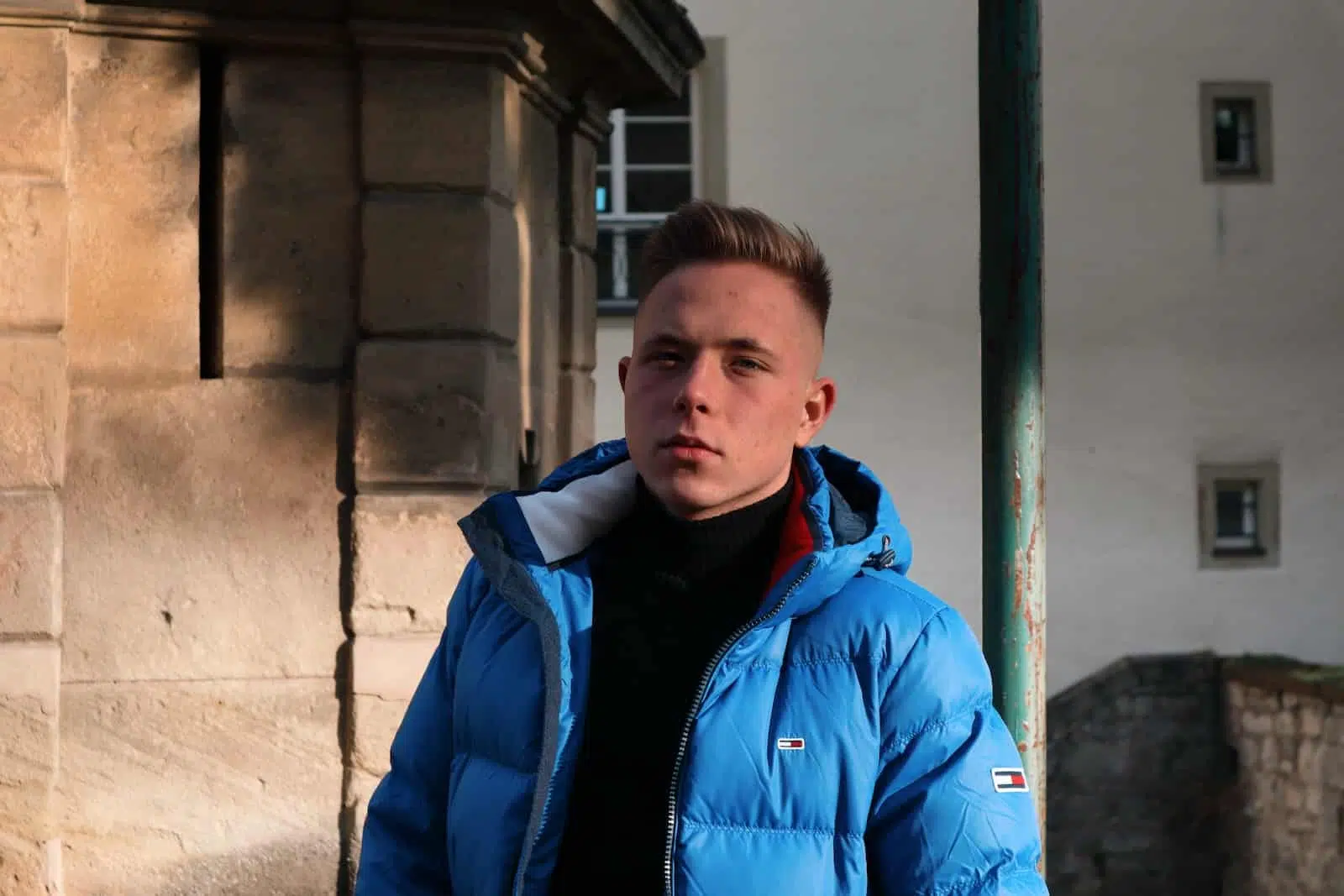 man in blue jacket standing beside brown concrete wall during daytime