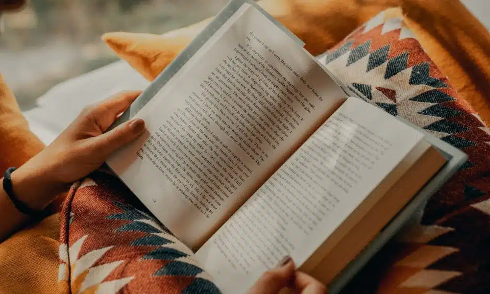 person reading book on brown and beige textile