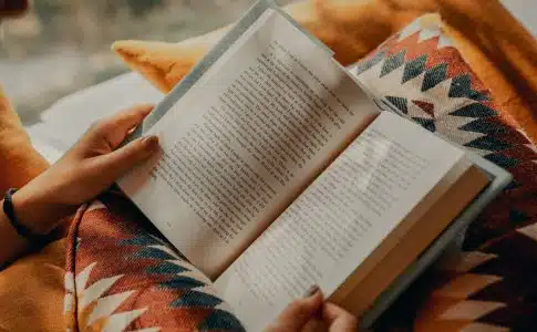 person reading book on brown and beige textile